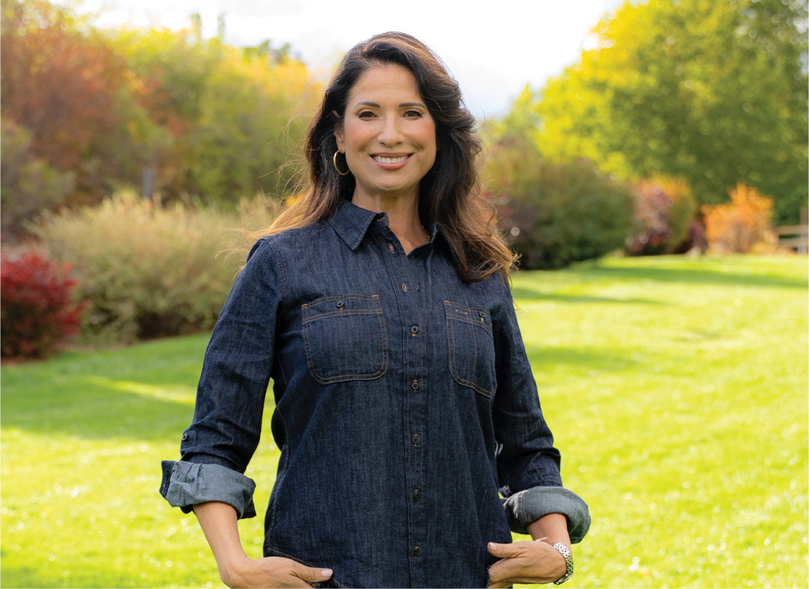 Adriana Guzmán Fralick smiling in front of a yard of grass and plants